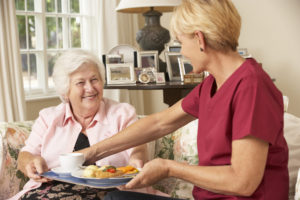Helper serving senior woman a meal.